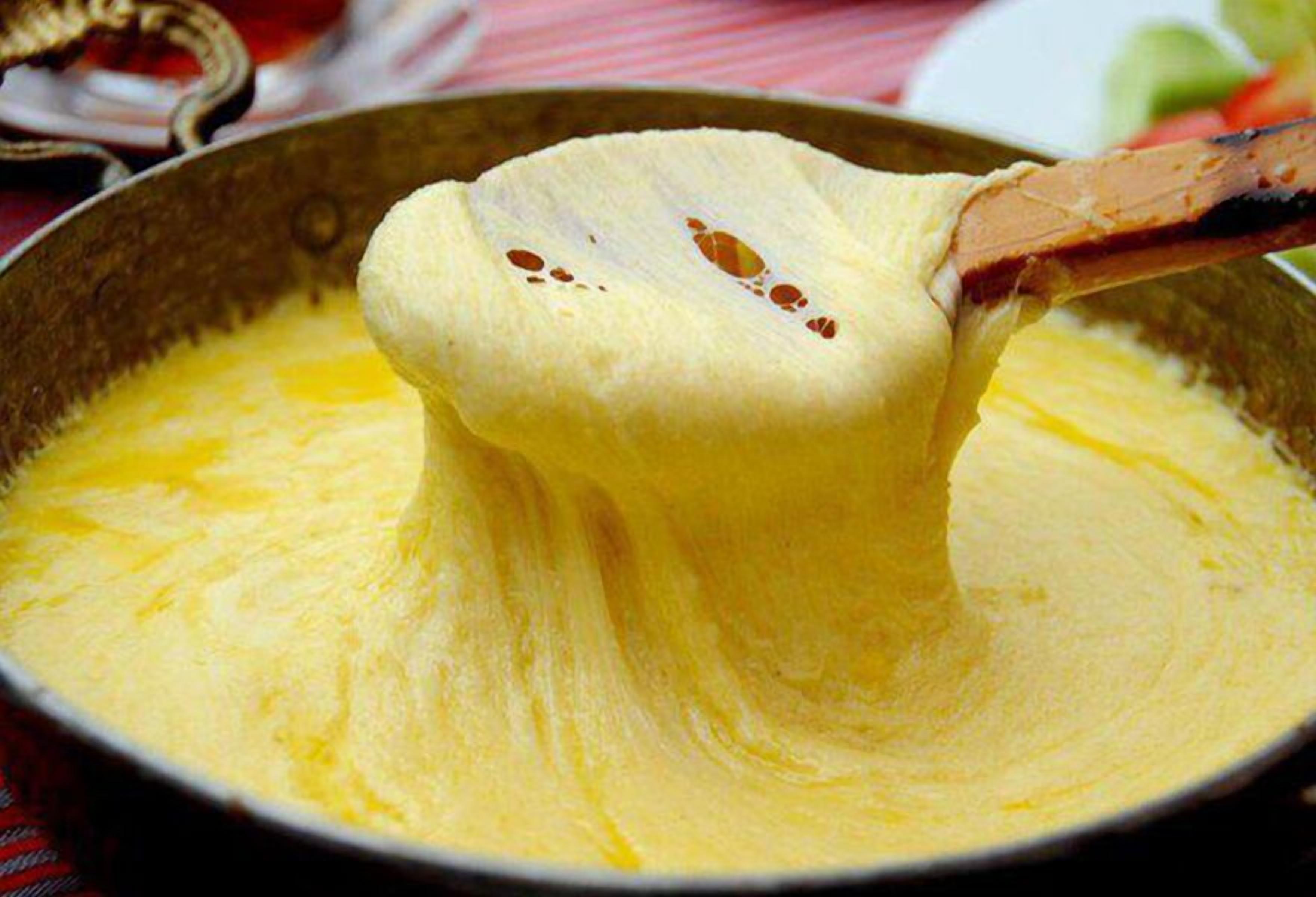 A close-up of a creamy, yellow substance being lifted from a pan.
