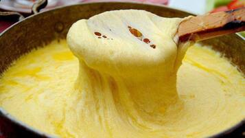 A close-up of a creamy, yellow substance being lifted from a pan.