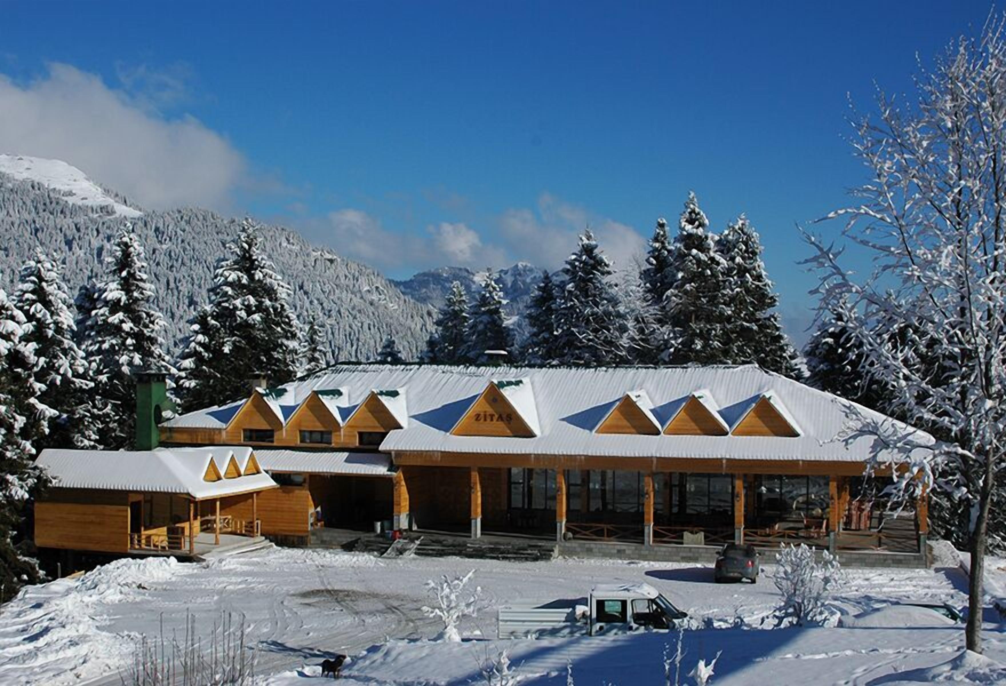 A lodge with a snow-covered roof and wooden exterior, surrounded by snow-covered trees and mountains.