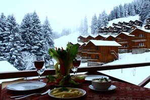 A dining table with a meal set, a glass of red wine, and a view of snow-covered cabins in the background. - Hamsiköy Zitaş Otel & Bungalov & Restoran (Maçka)