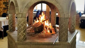 A stone-built fireplace with a fire burning inside, surrounded by stone arches, in a room with wooden ceiling and tiled floor. - Hamsiköy Zitaş Otel & Bungalov & Restoran (Maçka)