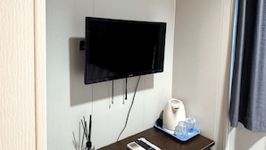 A hotel room with a mounted flat-screen TV, a small table with a kettle, glasses, and a remote control. - K Hotel 14 (Singapore)