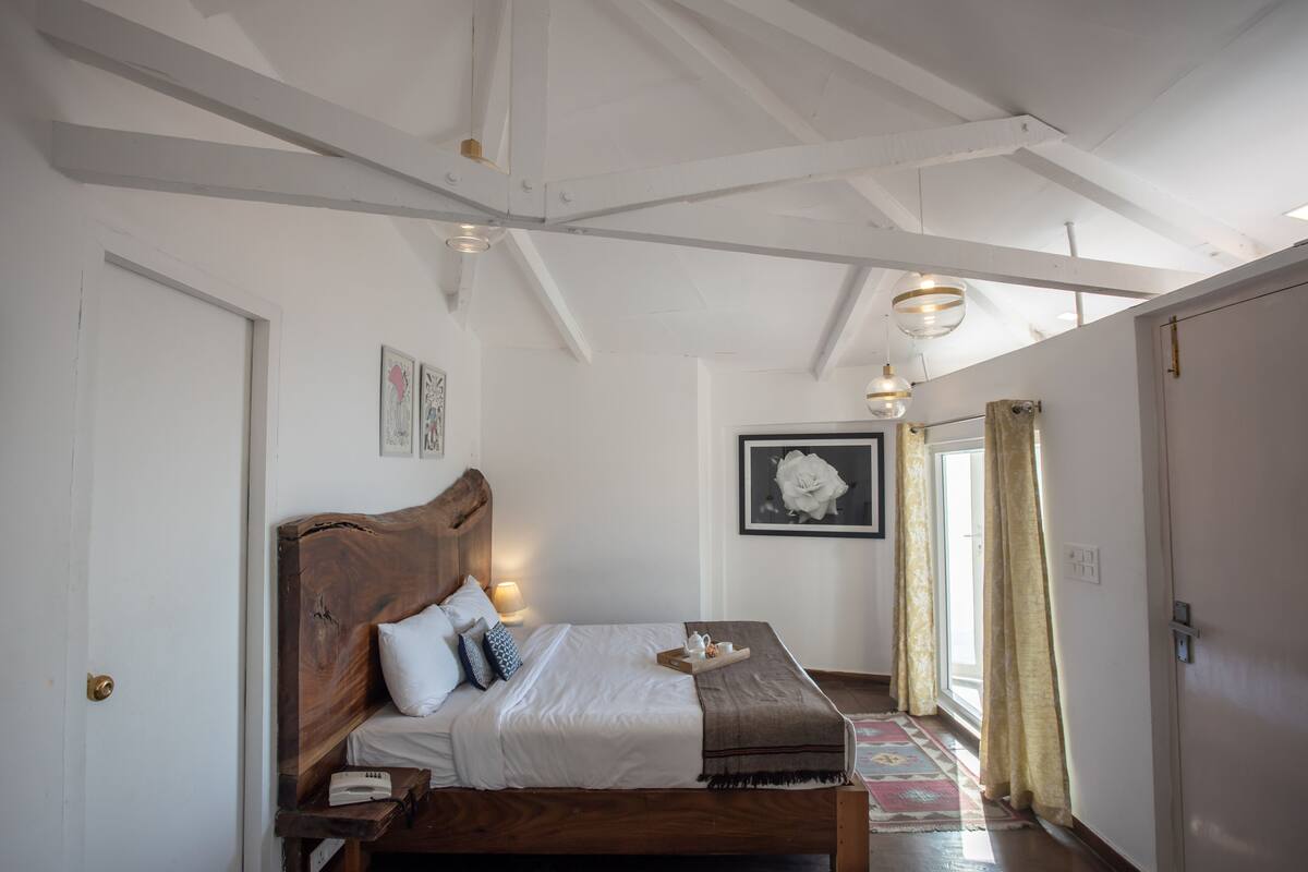 Une chambre à coucher avec un lit en bois, du linge de lit blanc, une table de chevet avec une lampe et un tableau encadré au mur.
