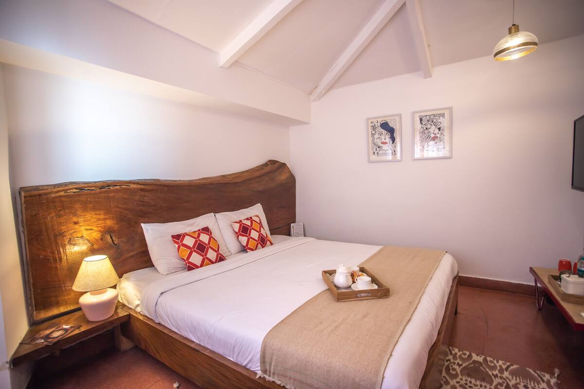 Un lit bien fait, avec une tête de lit en bois, une lampe de chevet et un plateau sur lequel se trouvent une théière et des tasses.