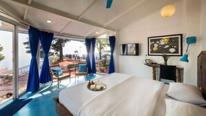 Une chambre d’hôtel avec un lit, un bureau, une chaise, un ventilateur de plafond bleu et une vue sur l’extérieur.