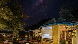 Un espace extérieur accueillant, aménagé avec des sièges confortables et une piscine, entouré de plantes en pot et équipé d’un écran de projection pour afficher une présentation.