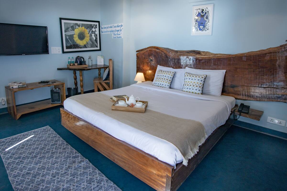 Une chambre avec un lit en bois, une table de chevet avec une lampe, un téléviseur fixé au mur et une citation encadrée au-dessus du lit.