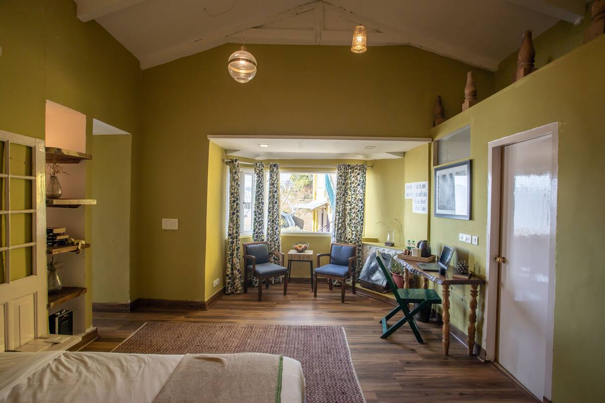 Une pièce spacieuse avec une grande fenêtre, un plancher en bois, un bureau avec un ordinateur et deux chaises.