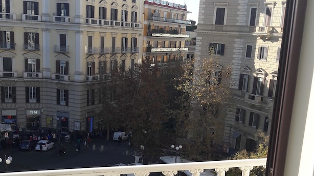 Ein Balkon mit Blick auf eine Stadtstraße, Gebäude und parkende Autos.