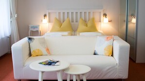 Un sofá blanco con almohadones amarillos y multicolores, dos mesitas blancas y dos lámparas fijadas a la pared.