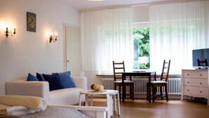 Habitación bien iluminada con cama, sofá, mesa de comedor con sillas, televisor y ventana con cortinas.