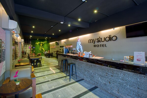 Eine moderne Hotelhalle mit einer Rezeption, einer Sitzecke und einem Neon-Schild für 'my studio hotel'.