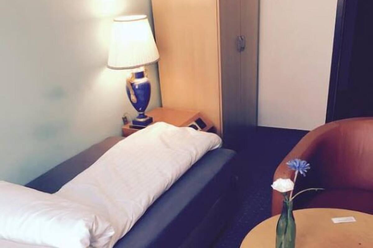 Ein Hotelzimmer mit einem Bett, einem kleinen Tisch, einem Stuhl, einer Lampe und einer Vase mit Blumen.