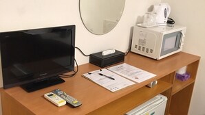 Un bureau dans une chambre d’hôtel, avec une télévision, des télécommandes, un four à micro-ondes, un petit réfrigérateur, une poubelle, un miroir et une machine à café.