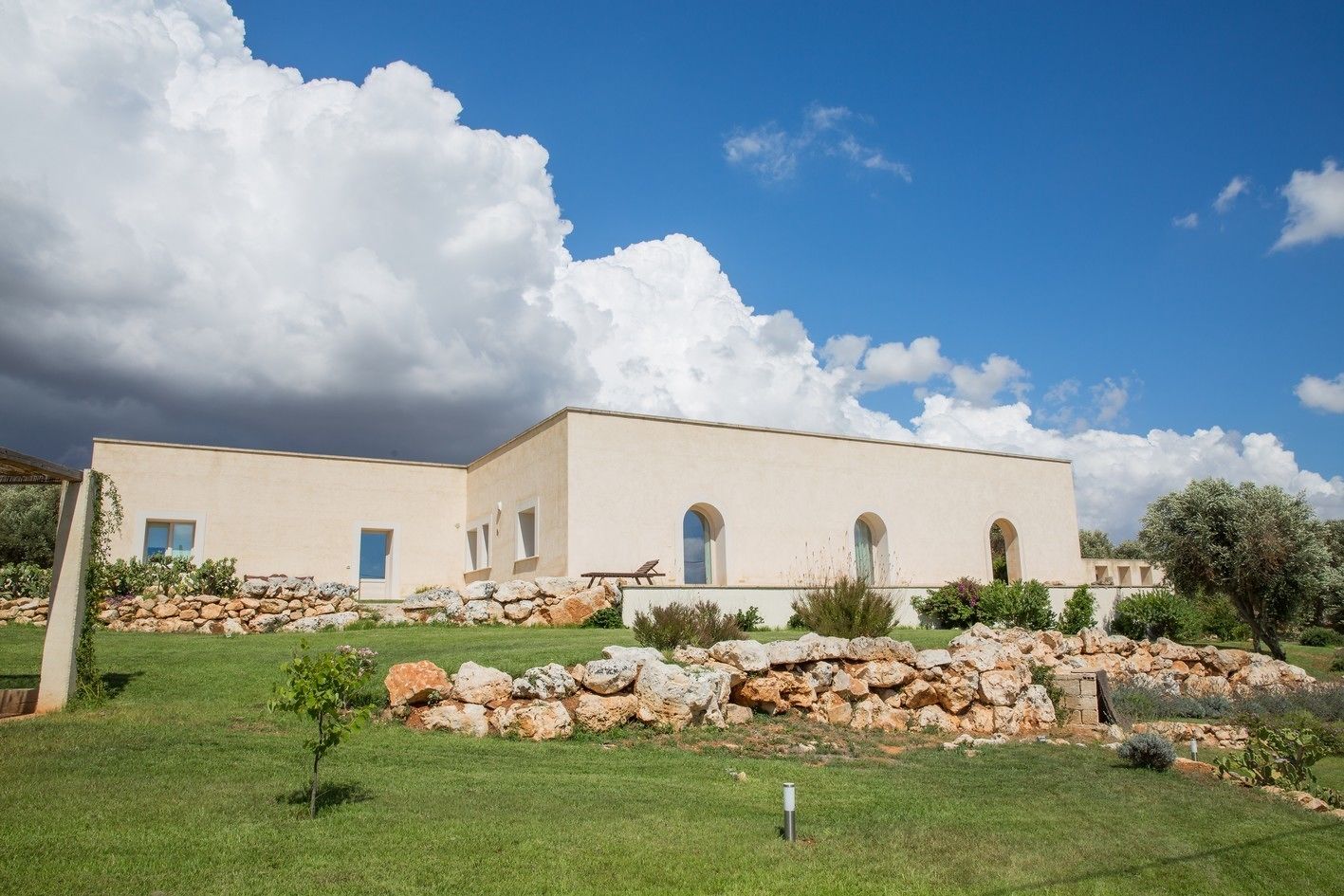 A modern building with a flat roof, large windows, and a stone wall in front.