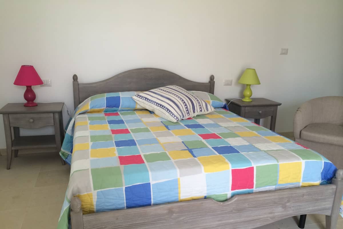 Une chambre à coucher avec un lit en bois, une courtepointe aux couleurs vives, deux tables de chevet avec des lampes et une chaise.