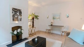 A modern living room with a fireplace, a coffee table, a sofa, and a dining area. - Bright and Leafy 1 Bedroom Flat in the Heart of Chelsea (London)