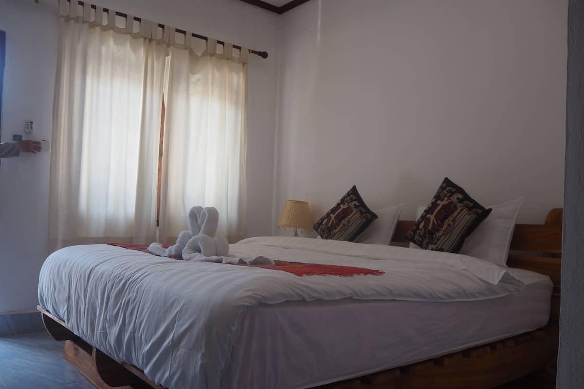 Una cama bien tendida con sábanas blancas, cabecera de madera y almohadas decorativas.