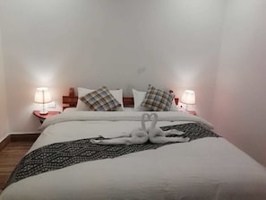 Ein ordentlich bezogenes Bett mit einer dekorativen Schwanen-Kissenanordnung, einer gemusterten Tagesdecke und Nachttischlampen auf Holznachttischen.