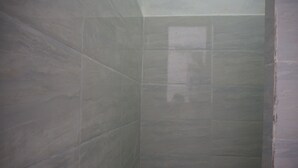 Um espaço de chuveiro pequeno e fechado, com paredes e chão revestidos de azulejos.