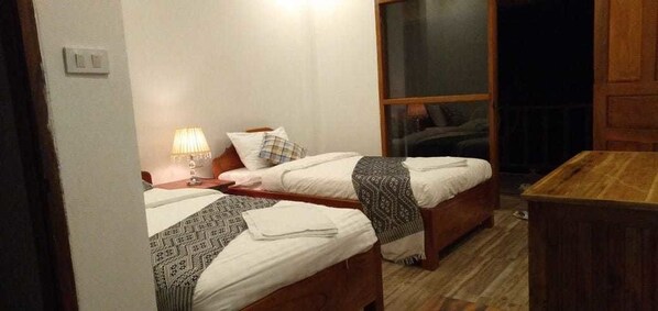 A room with two wooden beds, a nightstand with a lamp, and a wooden table.