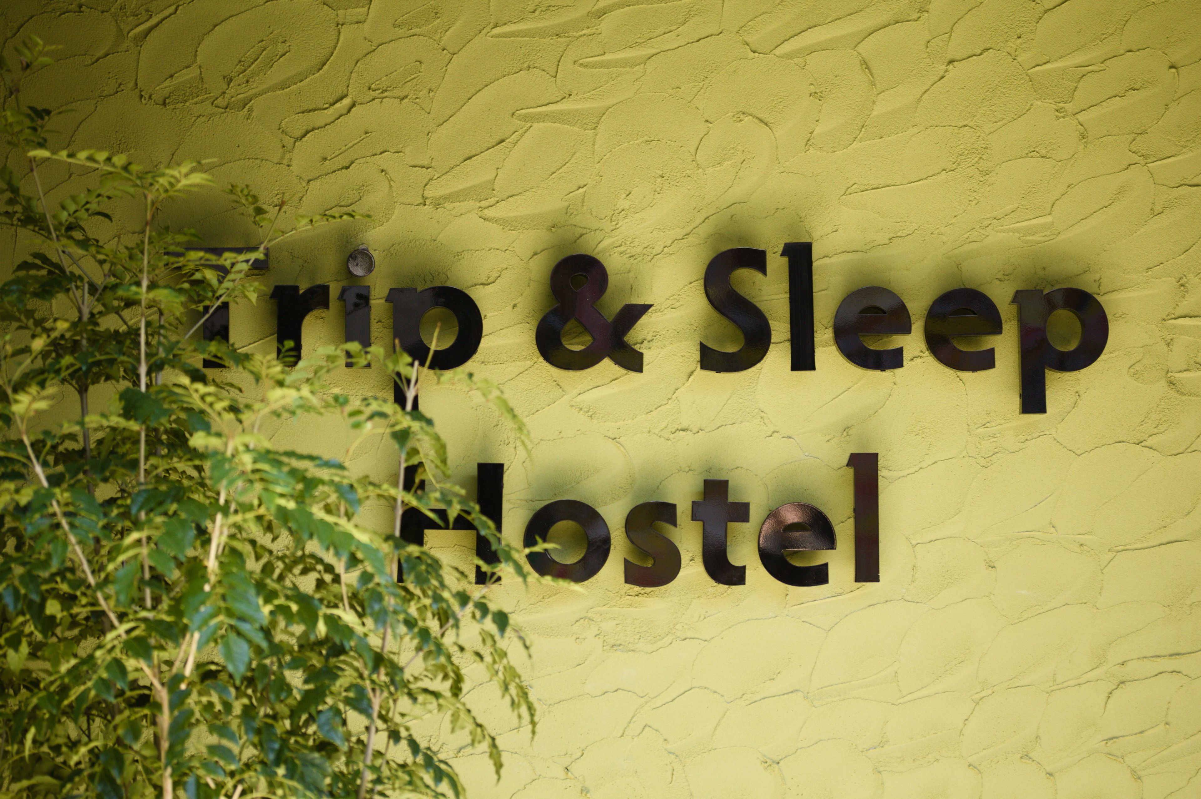 A sign for a hostel with the name "Trip & Sleep Hostel" on a textured yellow wall.