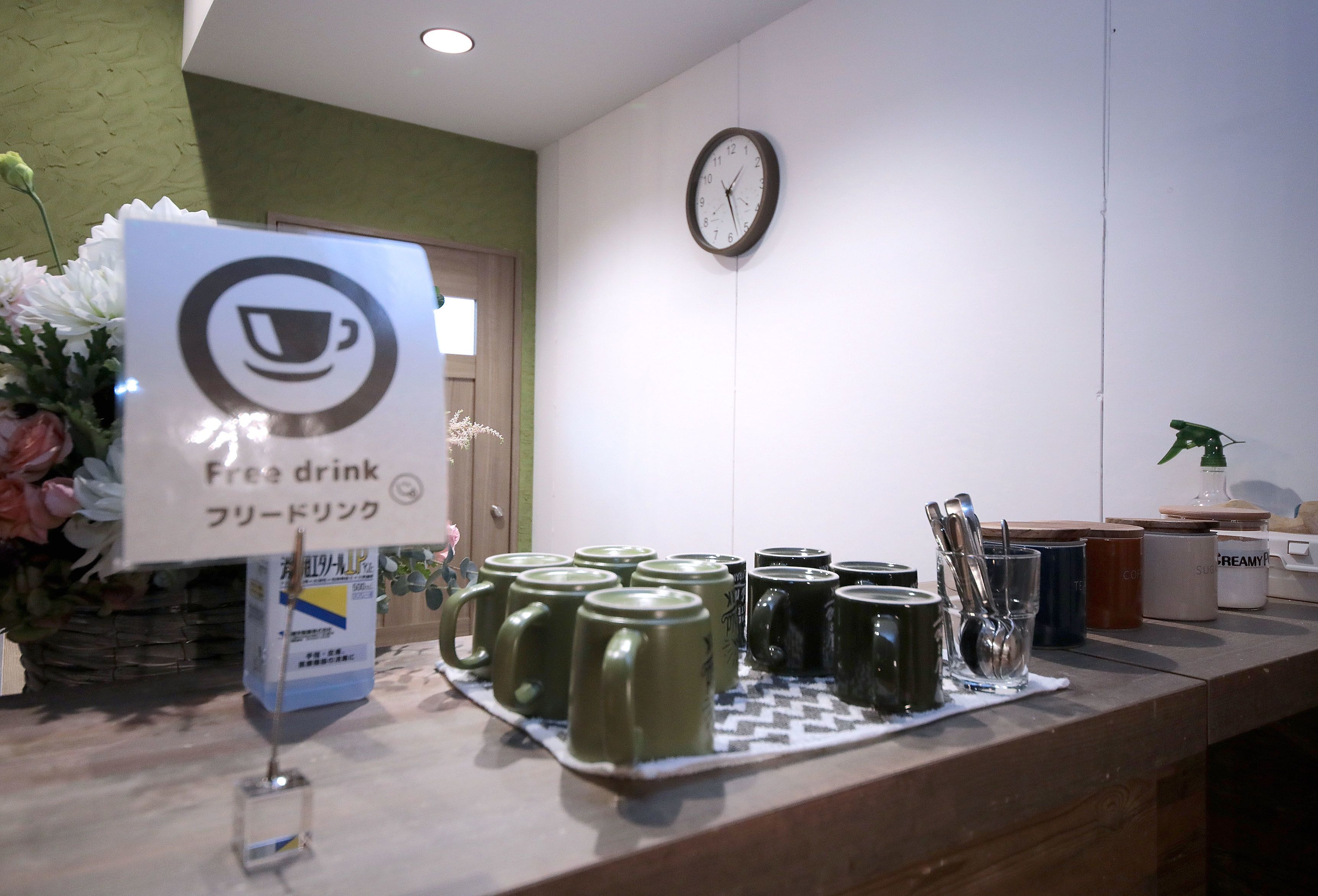 Un espace d’accueil avec une horloge, un panneau indiquant que les boissons sont offertes, et un plateau contenant des tasses et des couverts.