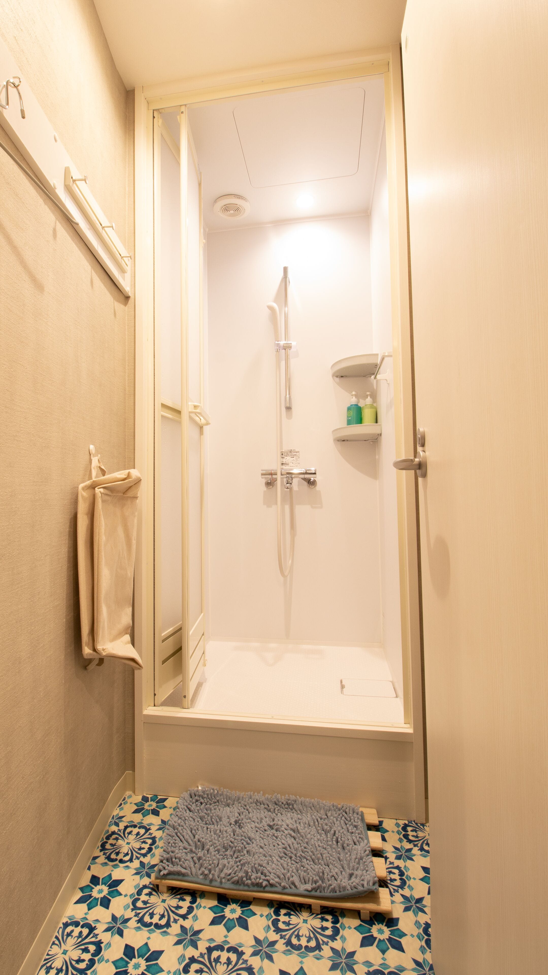 A small bathroom with a shower, a towel rack, and a shelf with toiletries.