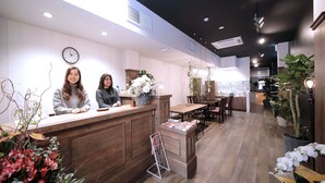 A reception area with a wooden counter, a clock, and a seating area with tables and chairs. - Trip & Sleep Hostel (Nagoya)