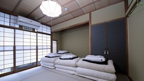 A traditional Japanese room with tatami flooring, a futon bed, sliding doors, and a ceiling-mounted air conditioner. - Trip & Sleep Hostel (Nagoya)