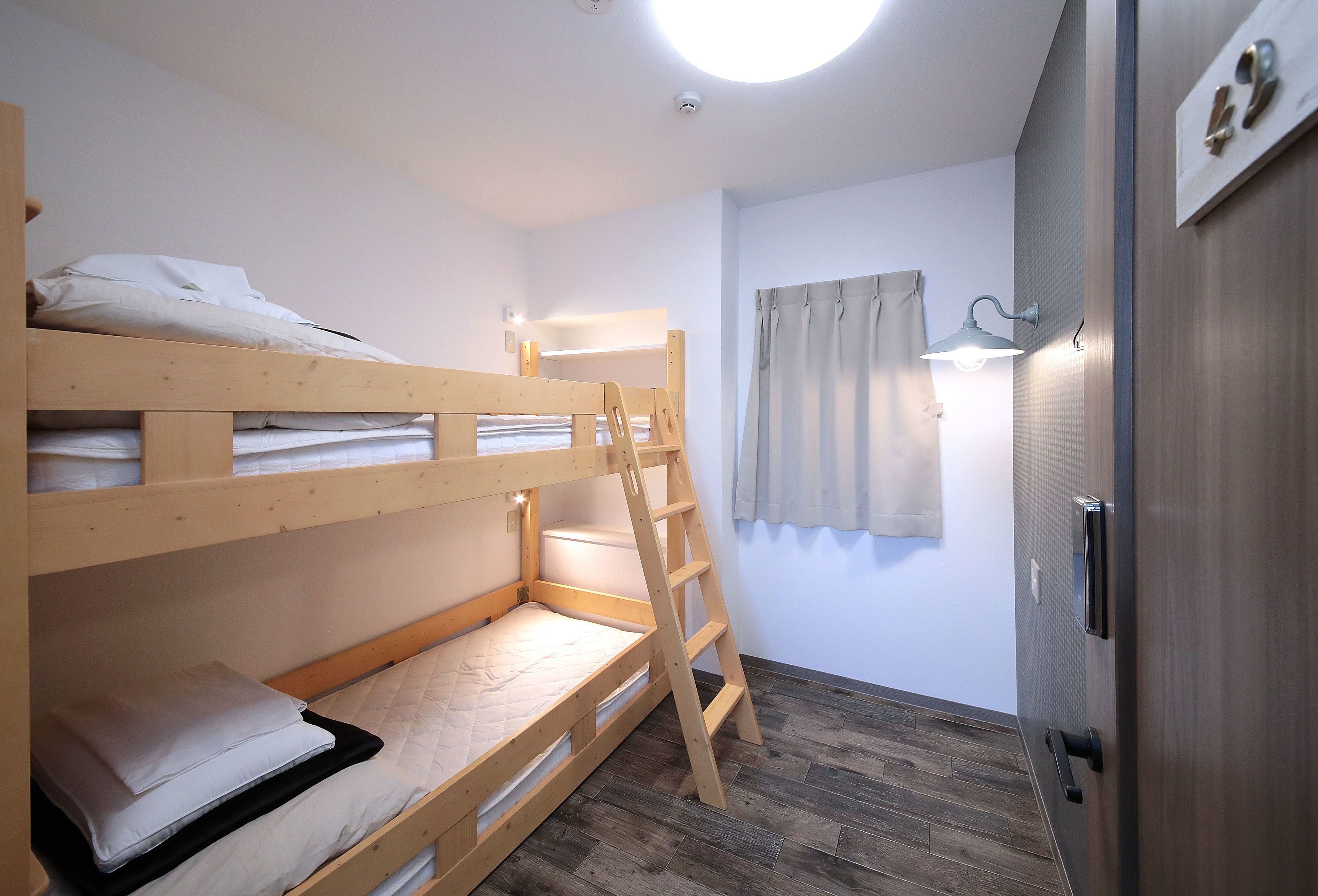 A bunk bed room with a ladder, a small window with curtains, and a door with a number plate.