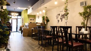 A restaurant with wooden tables and chairs, hanging lights, and potted plants. - Trip & Sleep Hostel (Nagoya)
