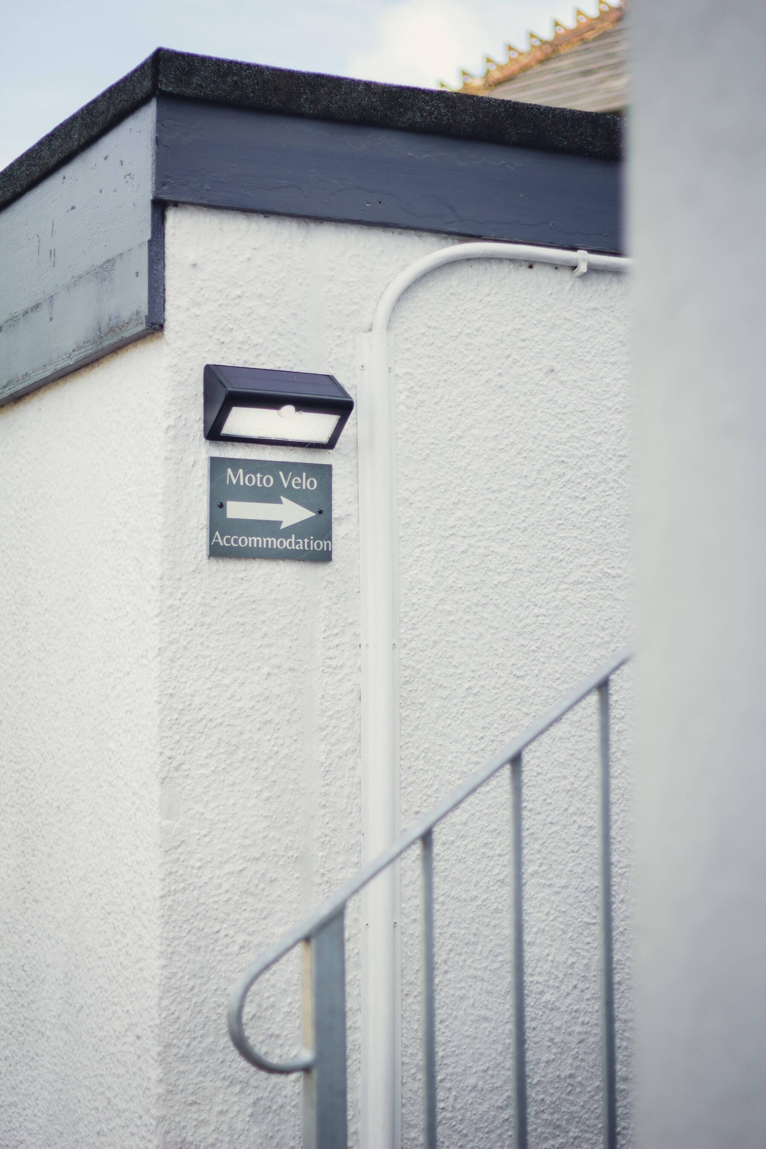 A sign on a white wall indicating 'Moto Velo Accommodation' with an arrow pointing to the right.