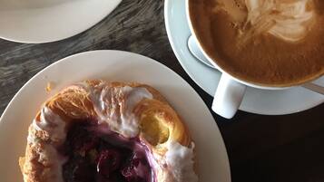 A breakfast setting with a croissant, a glass of orange juice, and a cup of coffee with latte art on a wooden table.