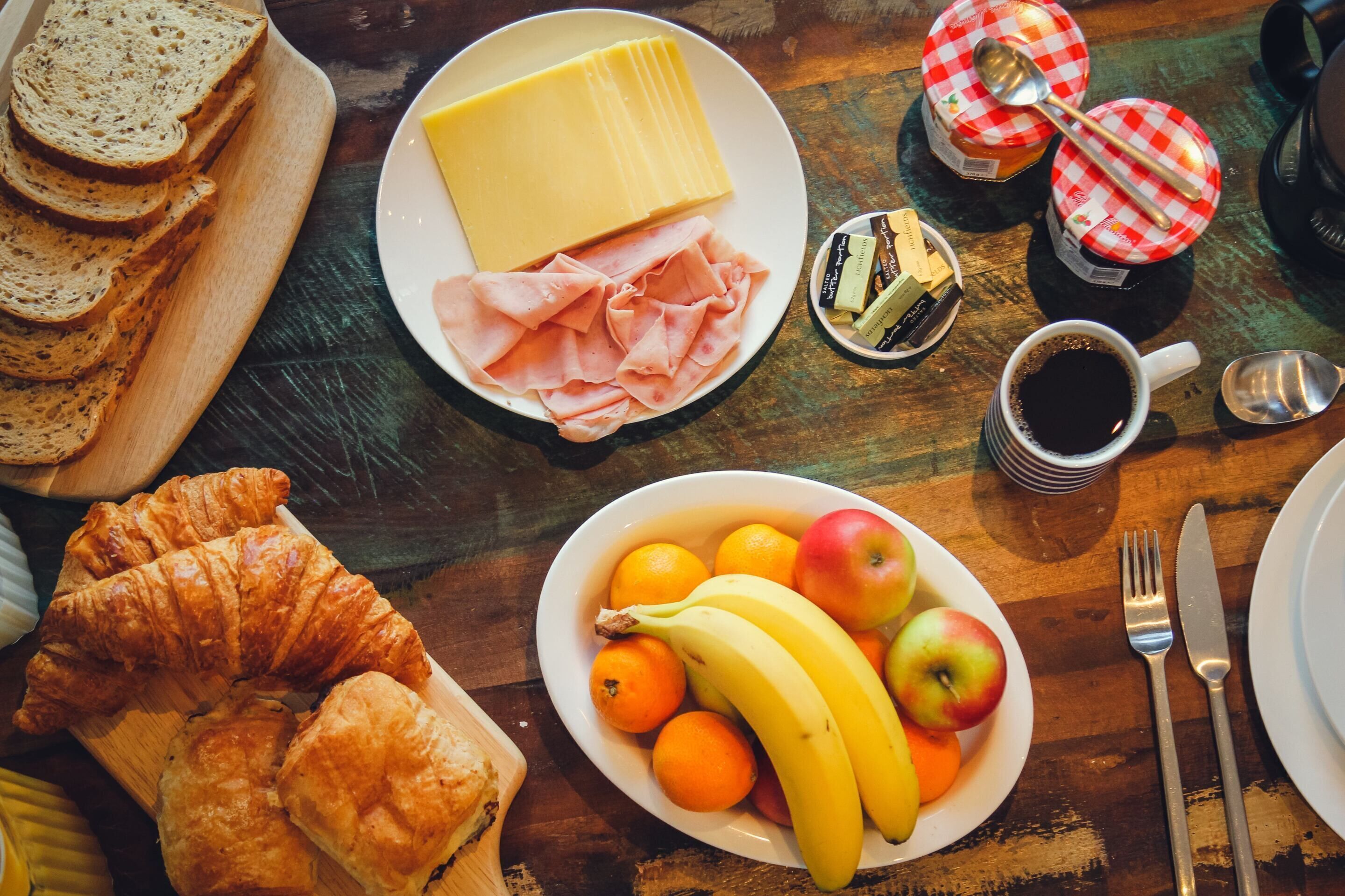 Un plateau de petit-déjeuner comprenant du pain, du fromage, du jambon, des croissants, des fruits et du café.