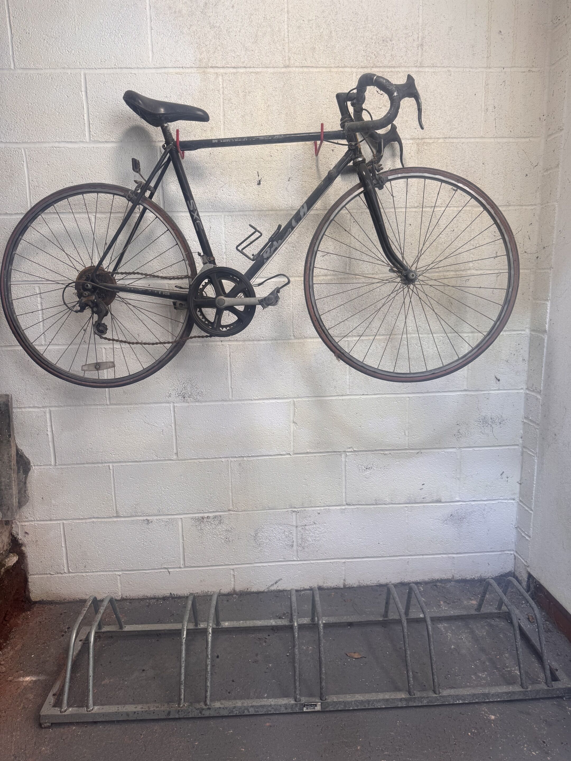 A bicycle leaning against a white brick wall with a metal rack below.