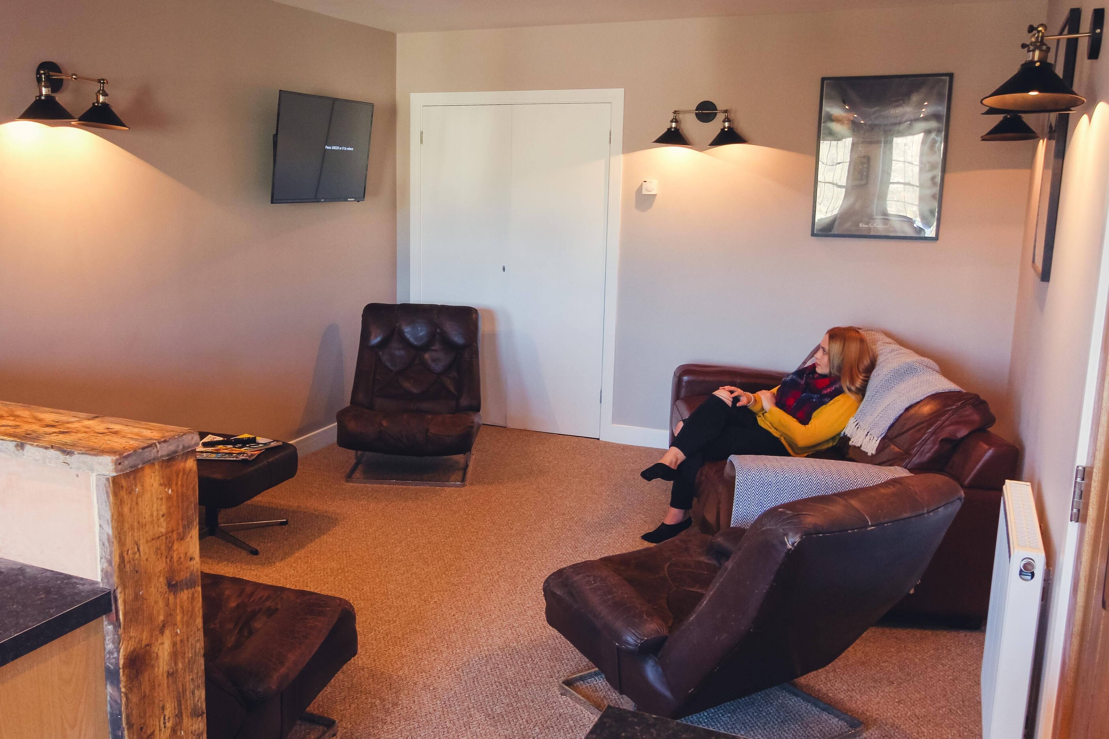 Una sala de estar con un sofá de cuero marrón, una mesa de centro de madera y un televisor de pantalla plana montado en la pared.