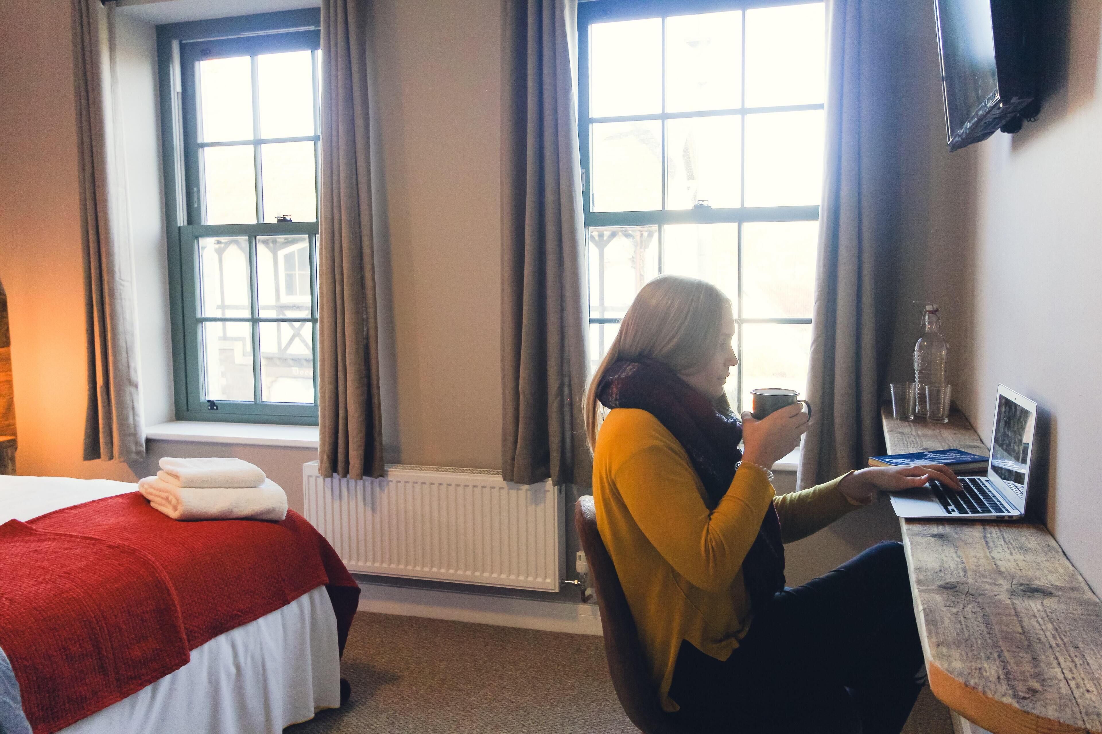 Una habitación de hotel con cama, un escritorio con una computadora portátil y una ventana con cortinas.