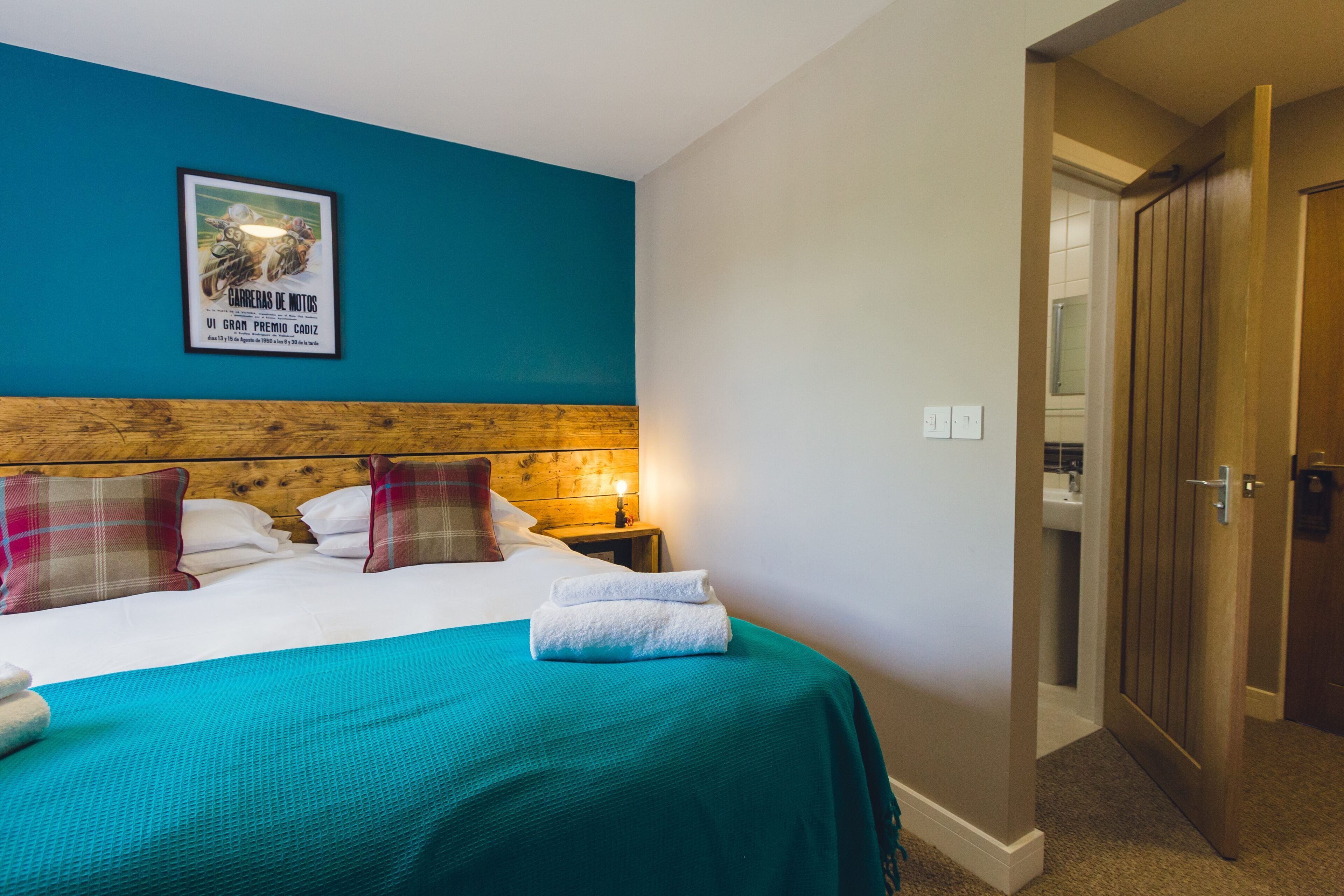 Una habitación de hotel con una cama, almohadas, un cuadro enmarcado en la pared y una puerta de madera.
