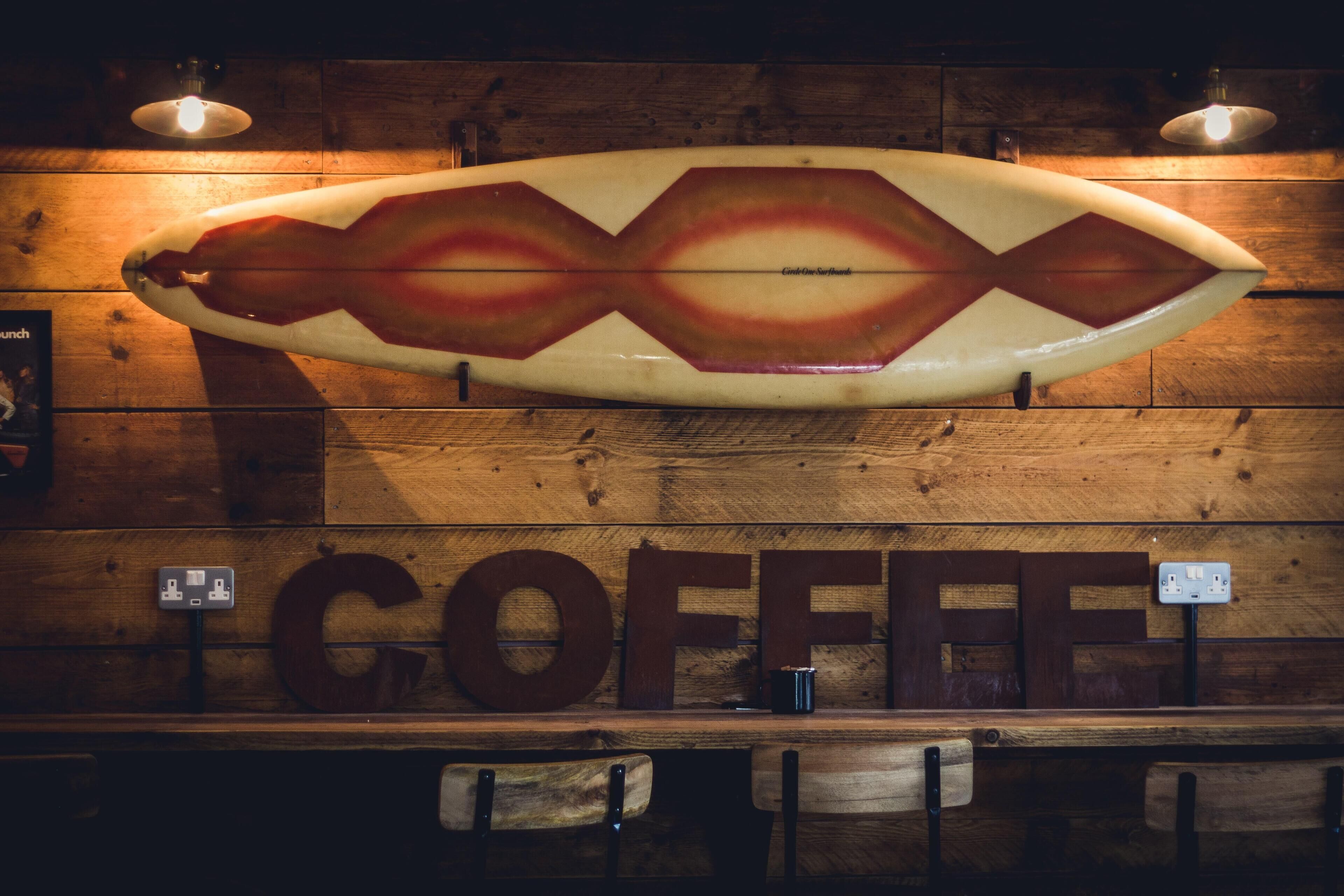 Una tabla de surf con un diseño único colgada en una pared de madera sobre un mostrador donde se lee la palabra "COFFEE".