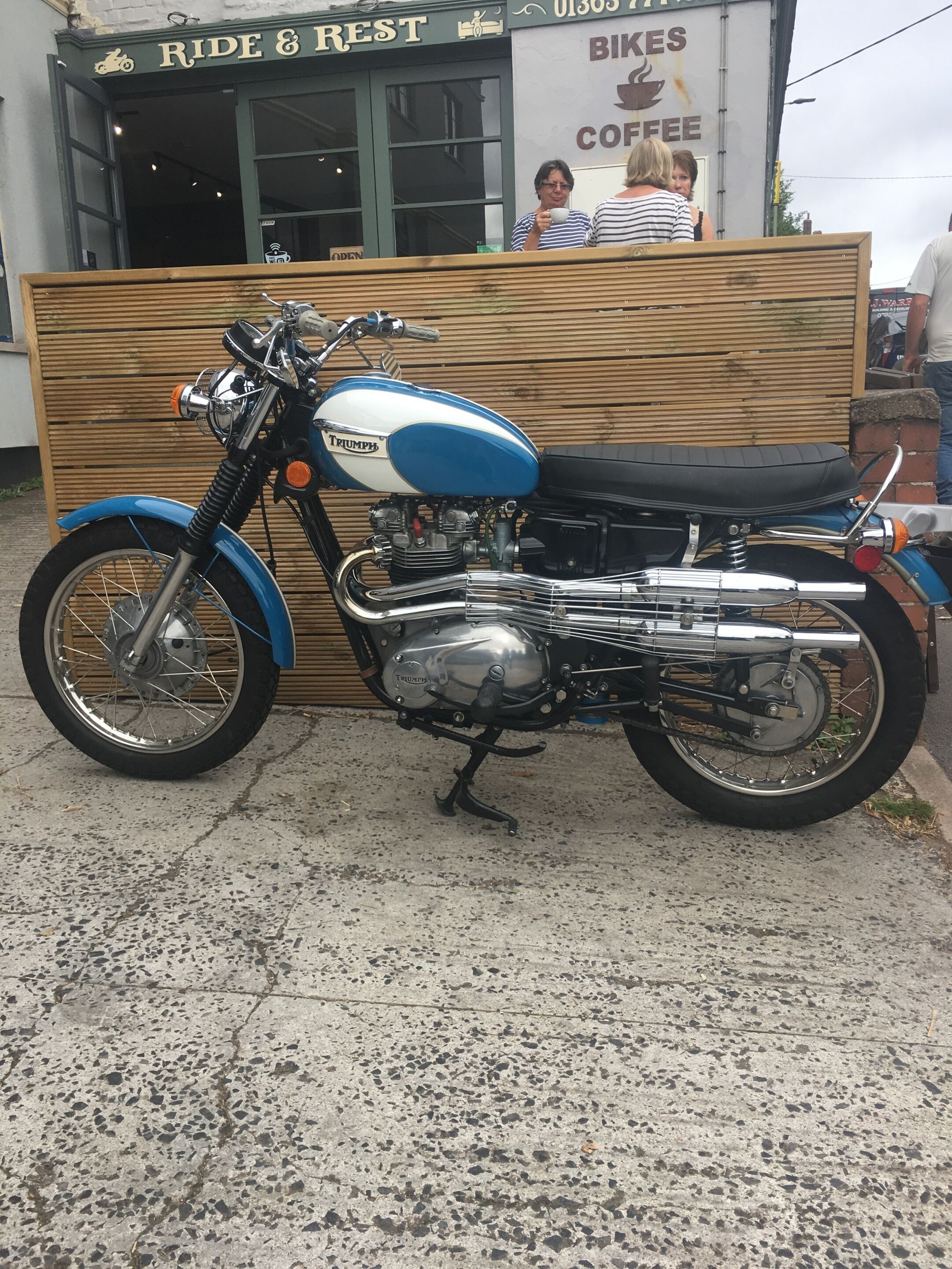 A Triumph motorcycle parked in front of a building with a sign that reads "Ride & Rest Bikes Coffee".