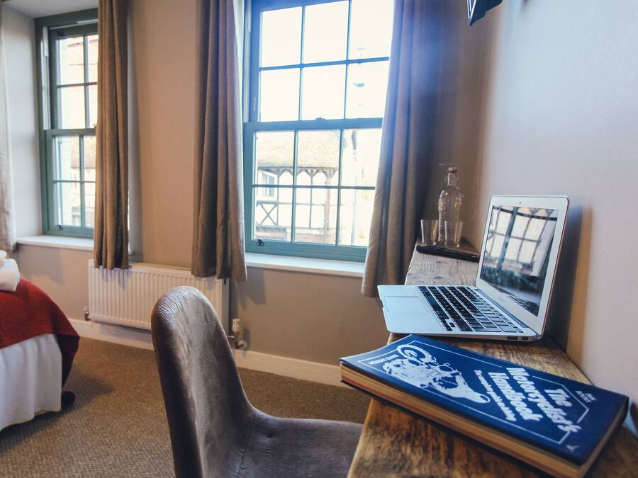 A hotel room with a bed, a desk with a laptop, a chair, and a window with curtains.