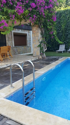 A swimming pool with a stone wall and a wooden deck.