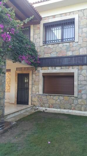 A stone house with a front door, a window with metal bars, and a covered patio area.