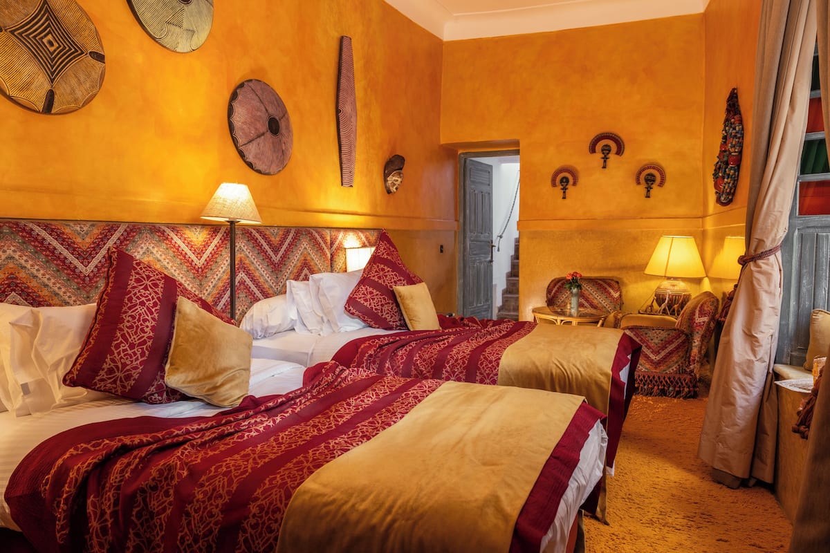 A hotel room with two beds, a large headboard, and a traditional decor style.