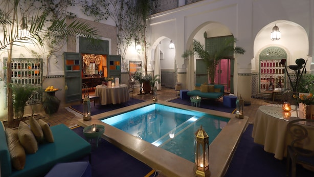 Un espace piscine intérieur luxueux, doté d’un coin salon et entouré d’arcades et de plantes.