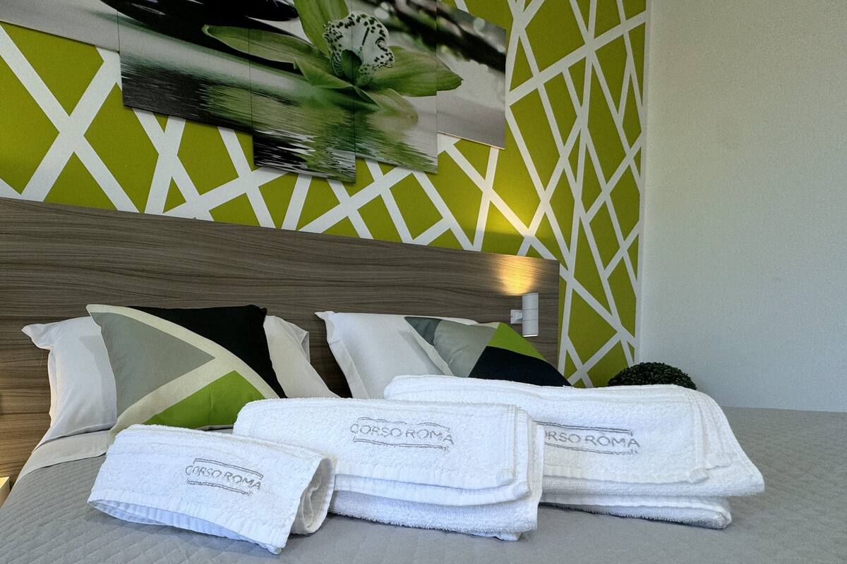 Un lit bien fait, avec des draps et des oreillers blancs, une tête de lit en bois et un motif géométrique vert et blanc sur le mur.