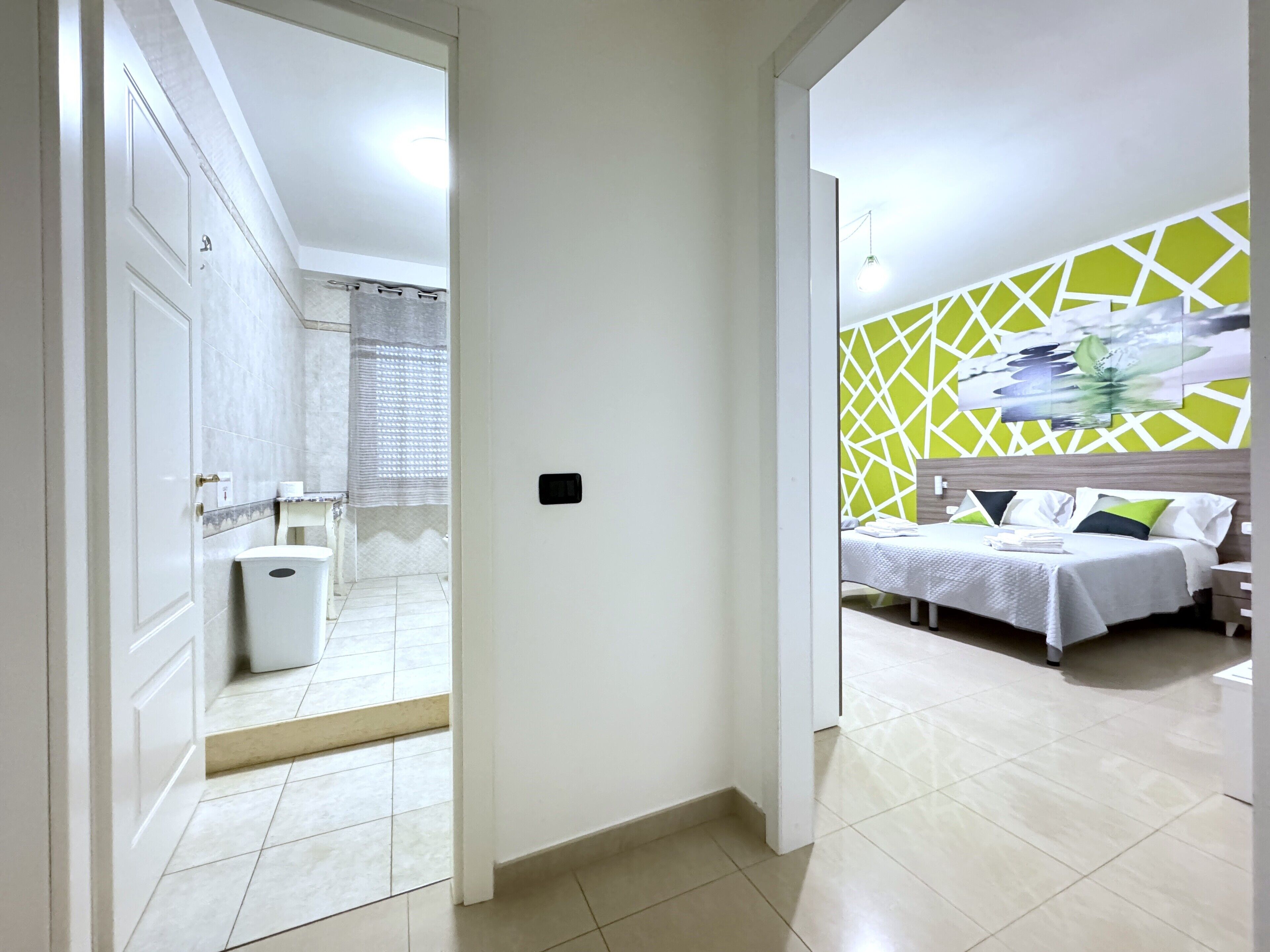 A hotel room with a bed, a nightstand, a wall-mounted artwork, and a bathroom visible through an open door.