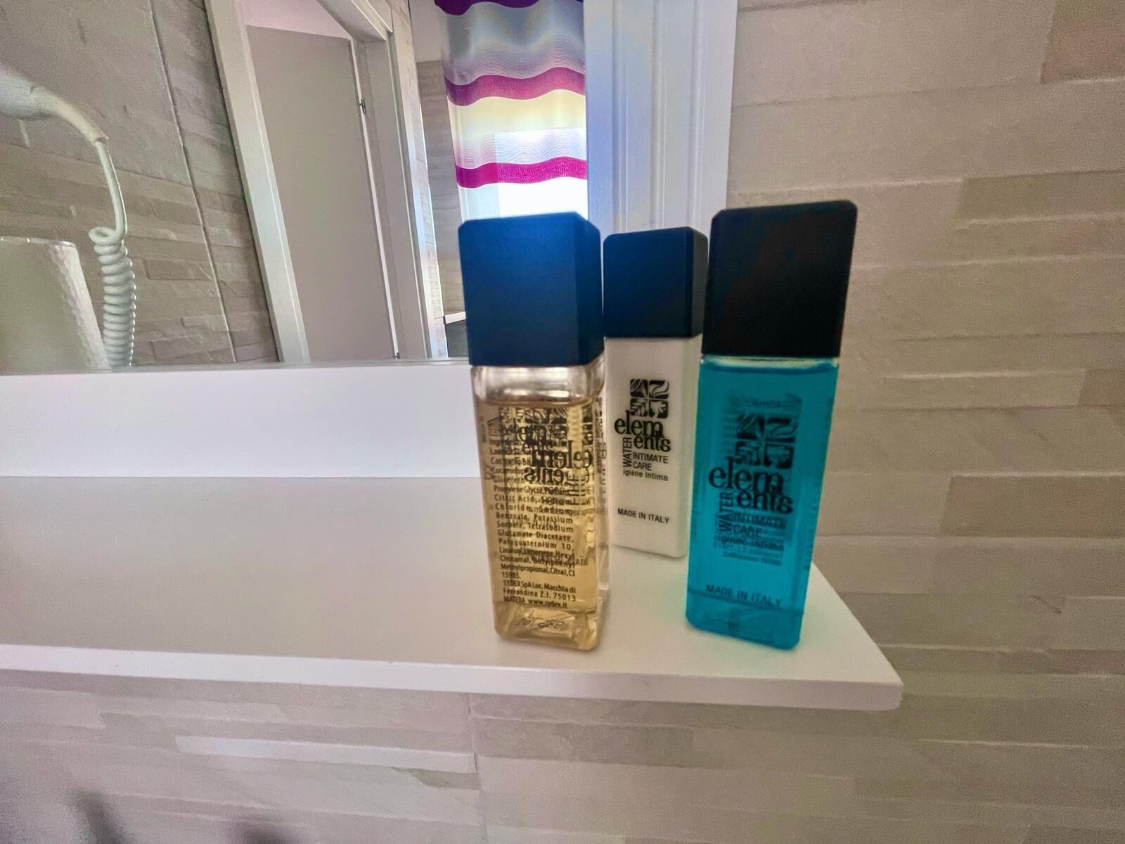 Trois flacons de produits de toilette sont posés sur une étagère blanche dans une salle de bain.