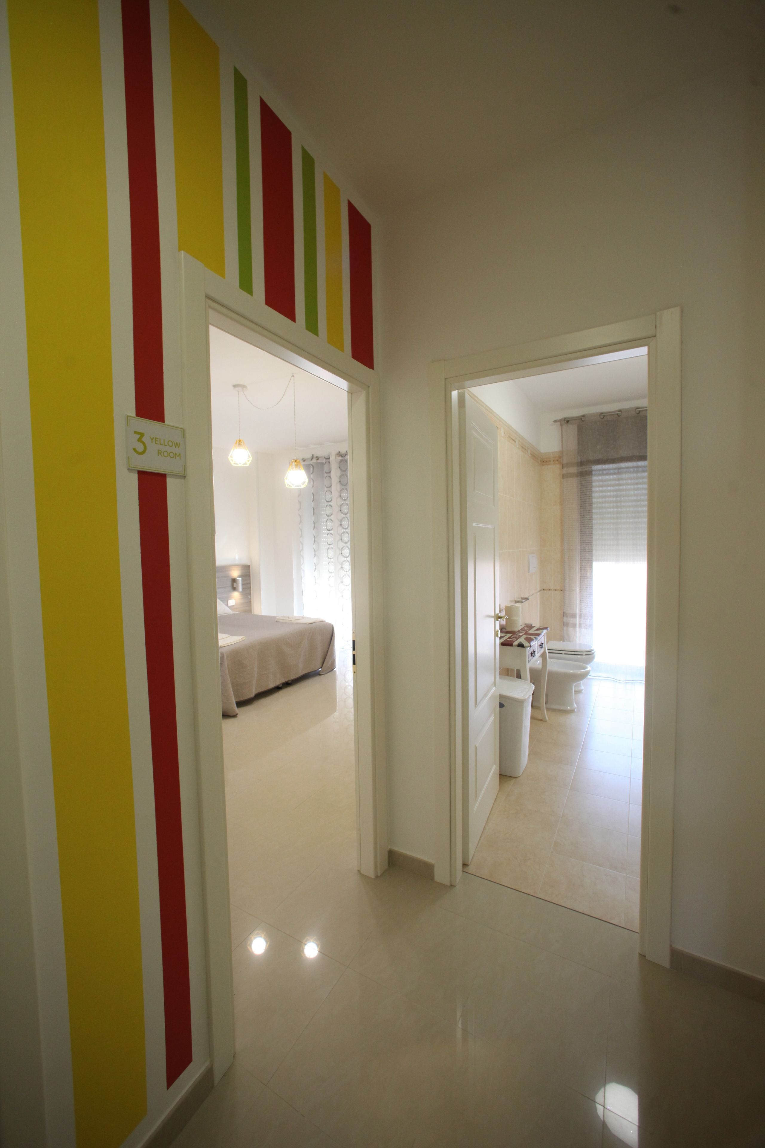 A hotel room with a bed, a bathroom with a toilet and sink, and a hallway with a sign indicating room number 3.